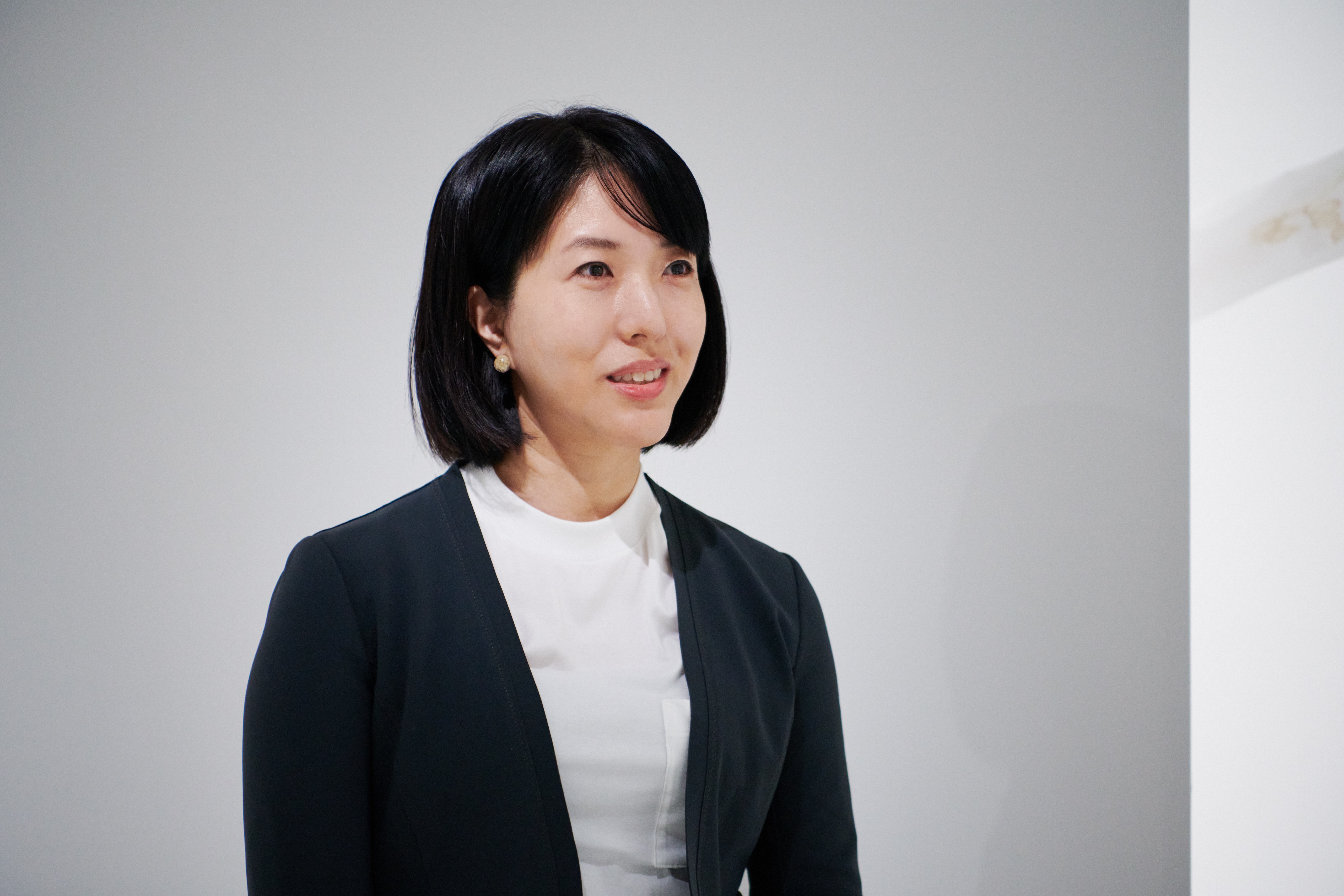 黒いジャケットを着た女性が、穏やかに微笑みながら少し右を見ています。